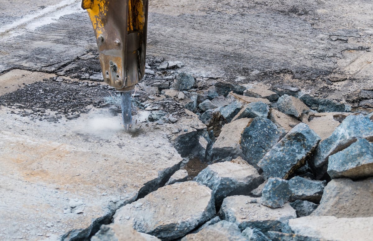 Hydraulic jackhammer on an excavator arm breaking up an old road