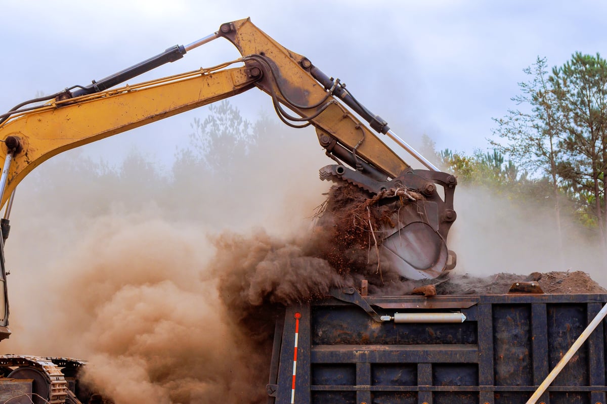 Heavy machinery lifting dirt and debris as dust clouds rise on a construction site
