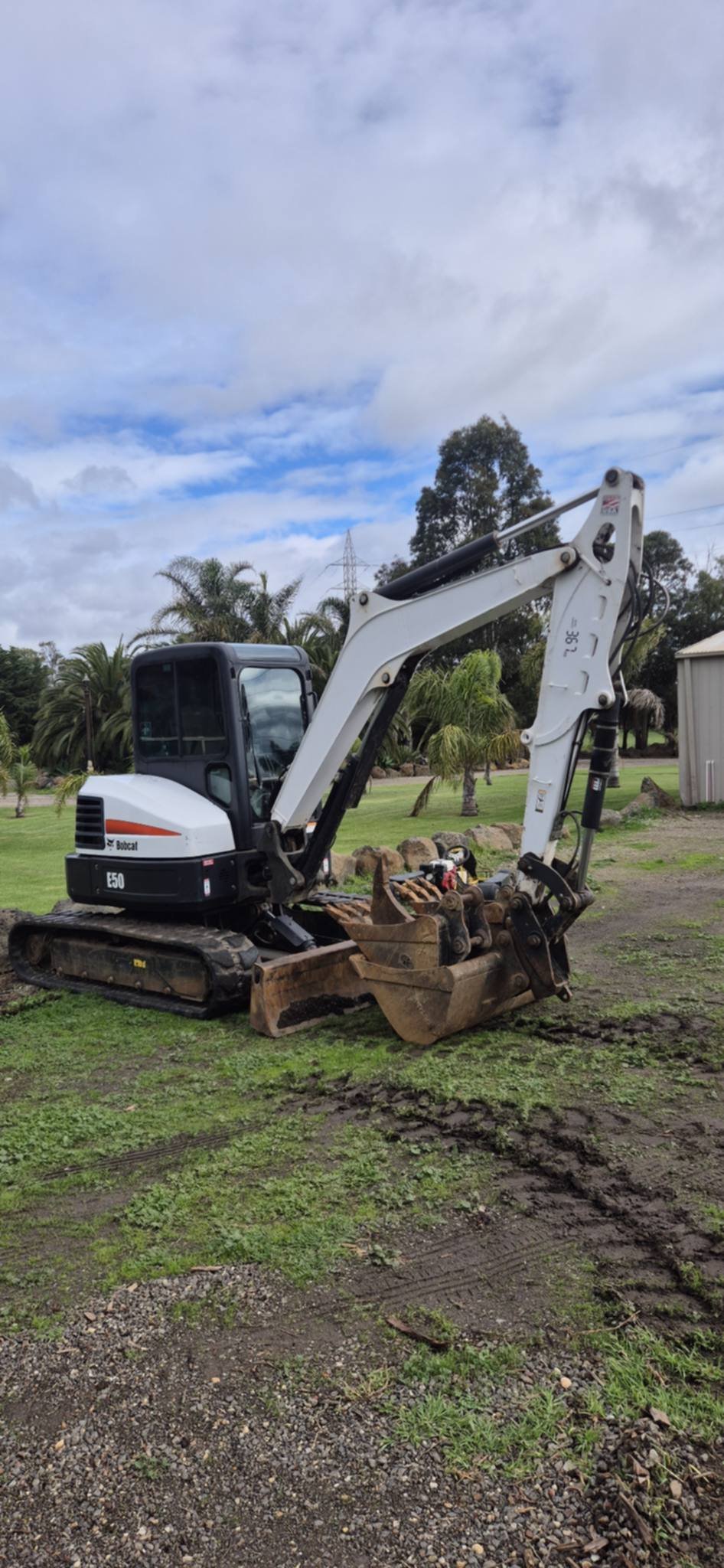 White and red mini excavator with bucket attachment on a rural grass property